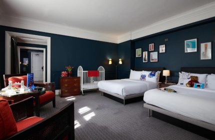The Dilly, gay-friendly hotel: Room with two beds, baby cot, dark blue walls, and London-themed decor. Ideal for gay men's family travel.