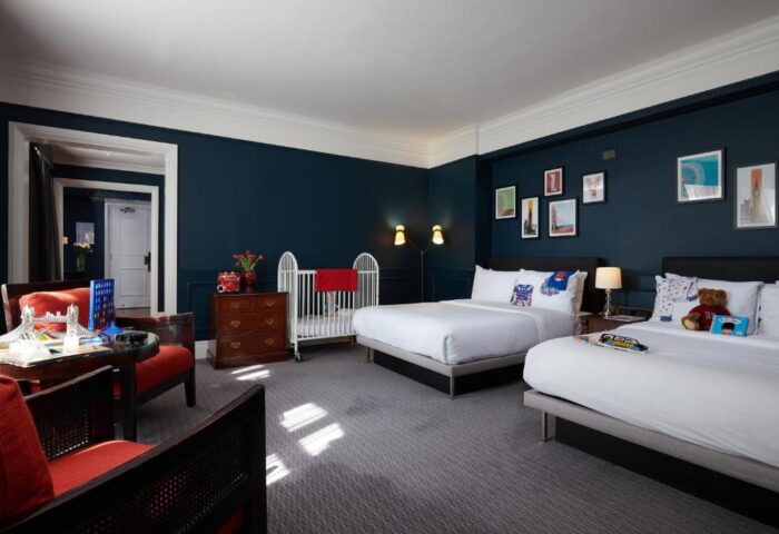 The Dilly, gay-friendly hotel: Room with two beds, baby cot, dark blue walls, and London-themed decor. Ideal for gay men's family travel.