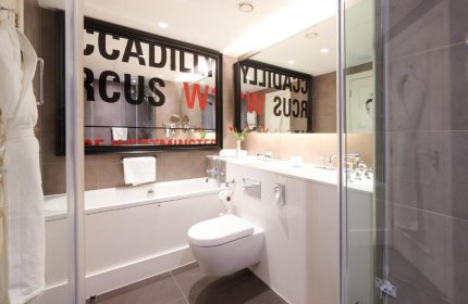 The Dilly, a gay-friendly hotel: Modern bathroom with tub, toilet, sink, and shower. Mirror reflects Piccadilly Circus W1. Ideal for gay travelers.