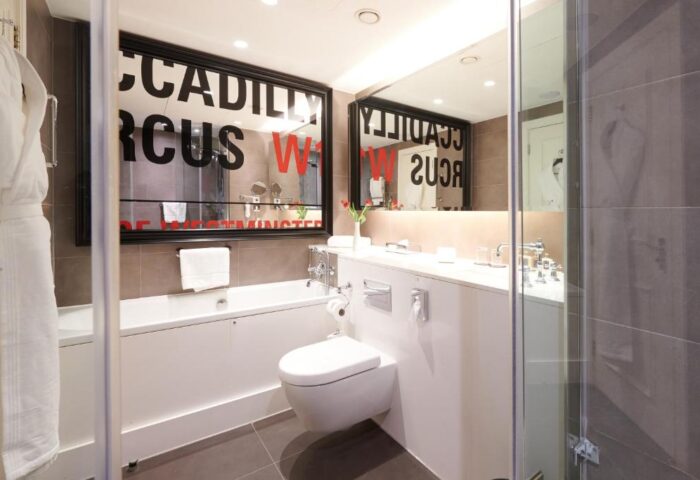The Dilly, a gay-friendly hotel: Modern bathroom with tub, toilet, sink, and shower. Mirror reflects Piccadilly Circus W1. Ideal for gay travelers.