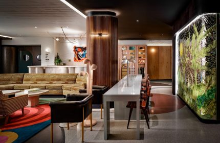 The Drake Hotel's gay-friendly interior features a stylish lobby with a retro sofa, long table, and colorful artwork. A welcoming space for travelers.