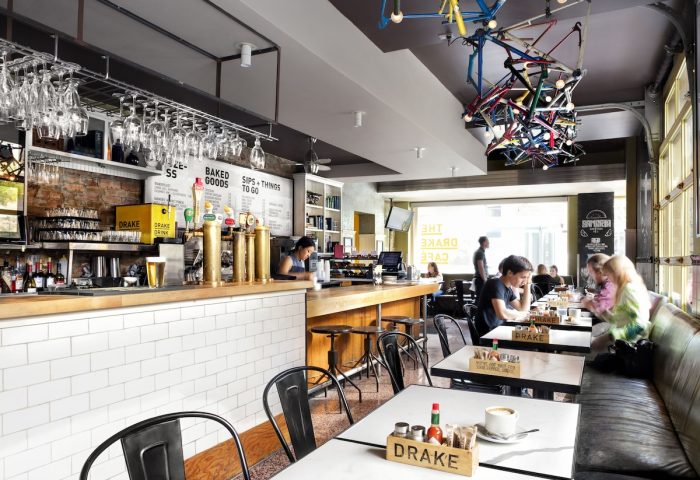 Interior of The Drake Hotel, a gay-friendly hotel. Bar with drinks, tables with people, and a bicycle frame chandelier. Great spot for gay men.