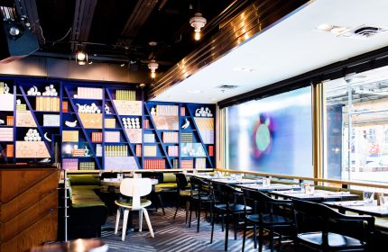 The Drake Hotel's gay-friendly restaurant interior. Blue bookshelf with objects, tables, and chairs. A stylish, welcoming space.