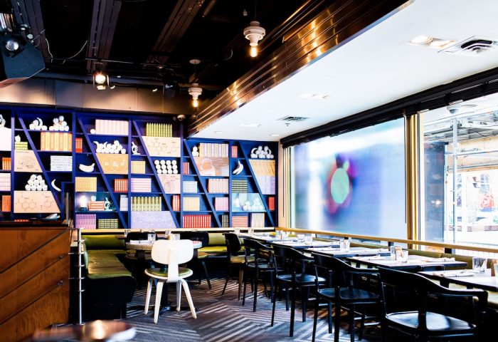 The Drake Hotel's gay-friendly restaurant interior. Blue bookshelf with objects, tables, and chairs. A stylish, welcoming space.