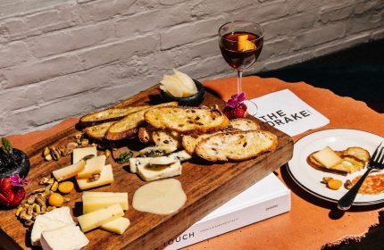 The Drake Hotel's gay-friendly ambiance: A charcuterie board with cheese, bread, nuts, and a cocktail. Cozy fireplace setting, perfect for gay travelers.