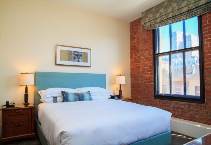 Fairmont Heritage Place Ghirardelli Square gay-friendly hotel room. Brick wall, large window, queen bed, and city view.