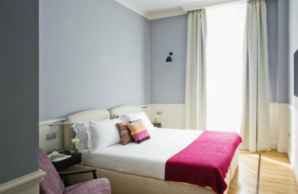 The Fifteen Keys Hotel room. Gay-friendly, pet-friendly hotel offers a cozy bedroom with a queen bed, colorful pillows, and a pink throw. Relaxing space.