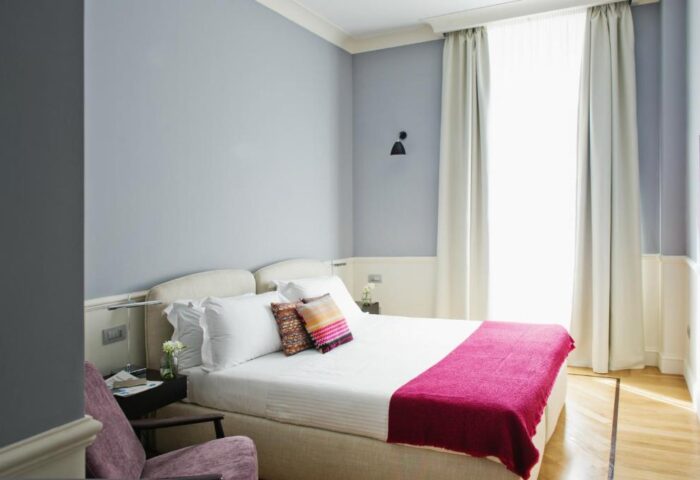 The Fifteen Keys Hotel room. Gay-friendly, pet-friendly hotel offers a cozy bedroom with a queen bed, colorful pillows, and a pink throw. Relaxing space.
