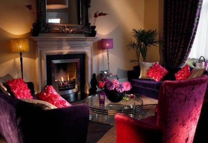 The Fleet, a gay-friendly hotel: cozy lounge area with fireplace, purple sofas, and red accents. A welcoming space for gay travelers.