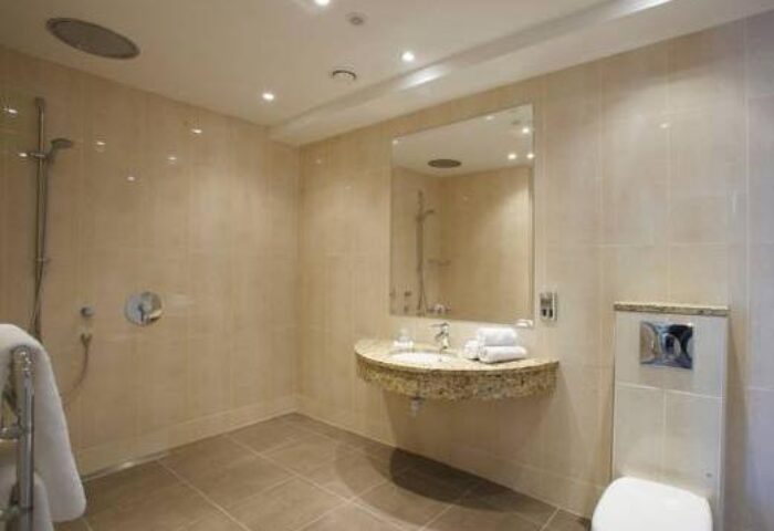 Bathroom at The Fleet, a gay-friendly hotel. Features a walk-in shower, tiled walls, sink, mirror, and toilet. Clean, modern design.