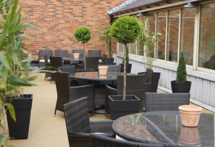 The Fleet's gay-friendly hotel patio. Outdoor seating area with wicker chairs, glass tables, and potted plants. A relaxing space for gay travelers.