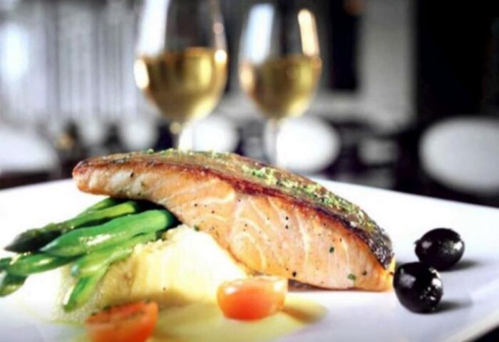 Fine dining at The Grove Suites by GRAND ASTON, a gay-friendly hotel. Salmon, asparagus, and wine create a luxurious experience.