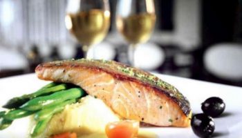 Fine dining at The Grove Suites by GRAND ASTON, a gay-friendly hotel. Salmon, asparagus, and wine create a luxurious experience.