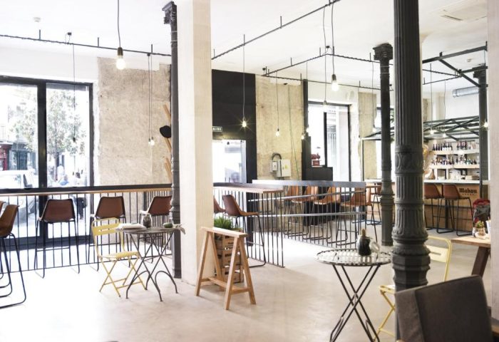 Interior of The Hat Hostel Madrid, a gay-friendly hotel. Bar with stools, tables, chairs, and industrial design elements.