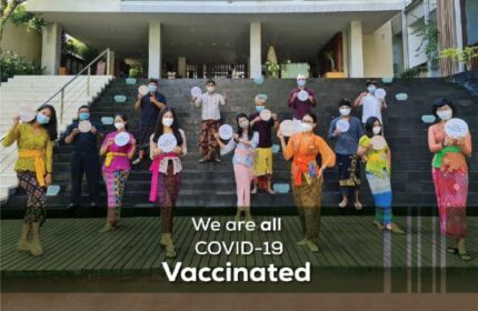 The Haven Bali Seminyak staff, a gay-friendly hotel, shows its COVID-19 vaccination status. Balinese attire, masks, and signs are visible.