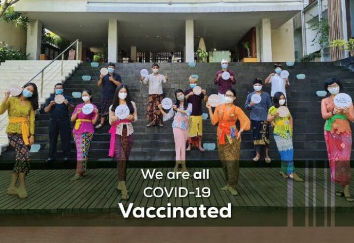 The Haven Bali Seminyak staff, a gay-friendly hotel, shows its COVID-19 vaccination status. Balinese attire, masks, and signs are visible.