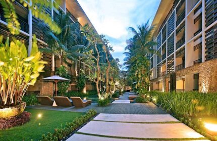 The Haven Bali Seminyak, a gay-friendly hotel. Lush courtyard view with lounge chairs, palm trees, and modern architecture in Seminyak, Bali.