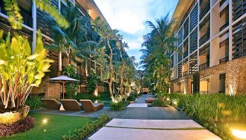 The Haven Bali Seminyak, a gay-friendly hotel. Lush courtyard view with lounge chairs, palm trees, and modern architecture in Seminyak, Bali.