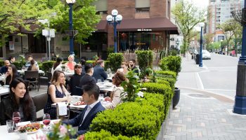 Outdoor patio at The Hazelton Hotel, a gay-friendly hotel. People dining, surrounded by greenery. Upscale Toronto street scene.