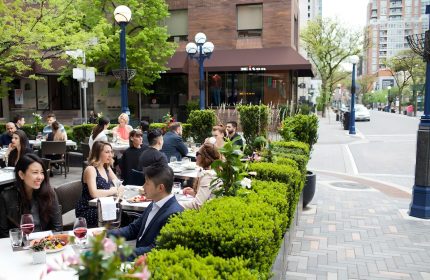 Outdoor patio at The Hazelton Hotel, a gay-friendly hotel. People dining, surrounded by greenery. Upscale Toronto street scene.