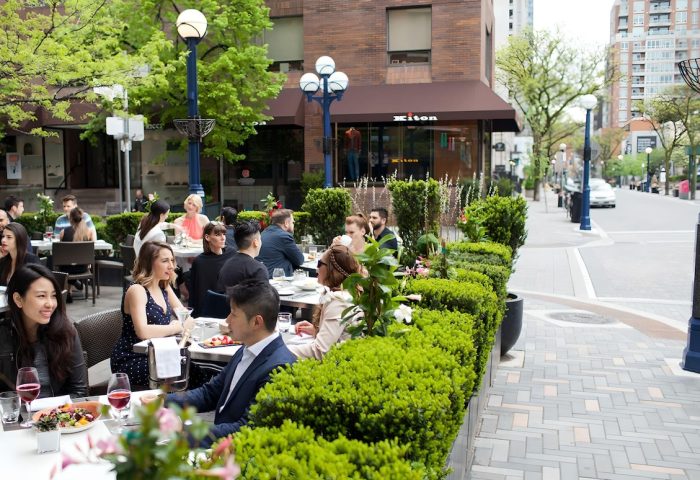 Outdoor patio at The Hazelton Hotel, a gay-friendly hotel. People dining, surrounded by greenery. Upscale Toronto street scene.