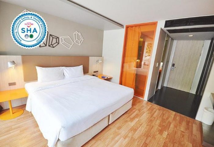 The Heritage Silom Hotel room. Gay-friendly hotel bedroom with king bed, wood floors, and orange accents. SHA certified for safety.