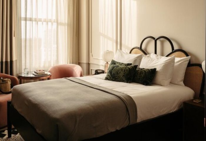 The Hoxton Downtown LA gay-friendly hotel room. A cozy bed with pillows, a throw, and a headboard. A chair and curtains add to the room's charm.