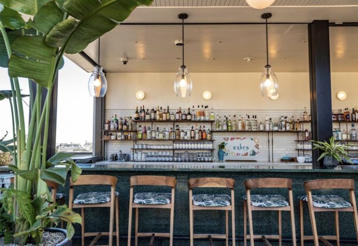 The Hoxton Downtown LA hotel bar. Stylish seating, lush plants, and a well-stocked bar create a welcoming vibe, perfect for gay travelers.