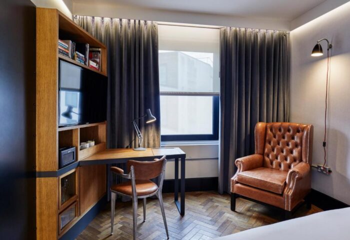 The Hoxton, Shoreditch hotel room. Desk and chair, leather armchair, herringbone floor, and window. Gay-friendly hotel for gay men travel.