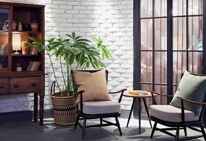The Hoxton, Shoreditch hotel interior. Cozy seating area with chairs, side table, and plant against a white brick wall. Gay-friendly hotel design.