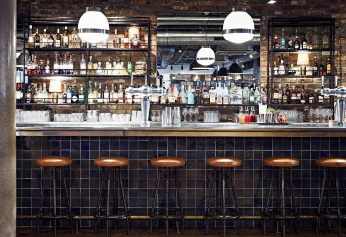 The Hoxton, Shoreditch gay-friendly hotel bar. Stools line the bar with bottles on shelves. A hip spot for gay travelers in London.