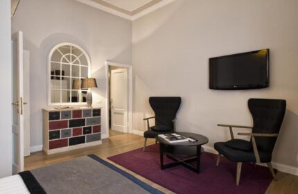 The Independent Suites gay-friendly hotel room. Lounge area with two chairs, table, TV, & colorful dresser. Gay travel advice.