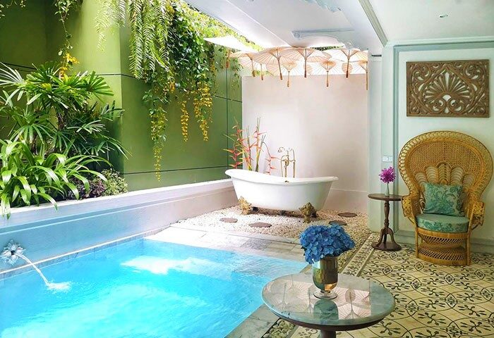 The Inside House gay-friendly hotel: Luxurious bathroom with pool, bathtub, plants, peacock chair. A relaxing space for gay men travel.