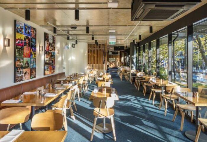 Interior of The Jazz Corner Hotel, a gay-friendly hotel. Tables and chairs are set for dining. Album art adorns the walls. Natural light floods in.