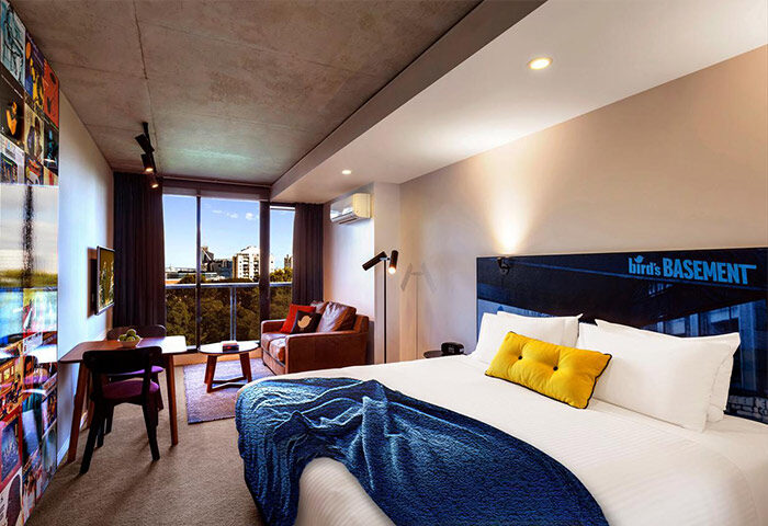 Gay-Friendly Hotel The Jazz Corner Hotel room. Modern design, bed with blue blanket, couch, city view. Gay travel lodging.