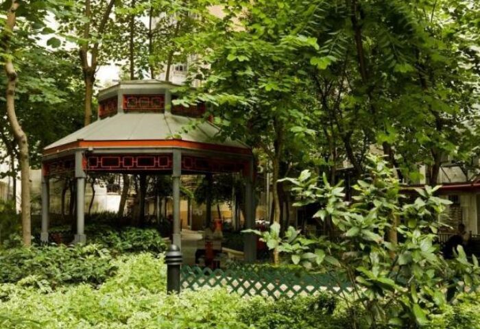 The Jervois gay-friendly hotel garden. A gazebo with gray columns and a red roof is surrounded by green trees and bushes. Serene outdoor space.