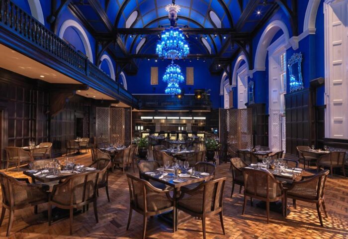 The Lalit London's restaurant. Gay-friendly hotel dining room with tables, chairs, blue walls, arched ceiling, and chandeliers. Fine dining.