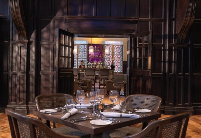 The Lalit London hotel's restaurant. A gay-friendly hotel with a bar and dining area. Table setting with glasses and silverware. Dark wood interior.
