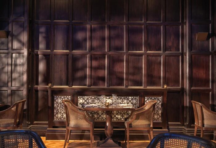 Intimate dining at The Lalit London, a gay-friendly hotel. Dark wood paneling, set table, and cane chairs create a warm, inviting atmosphere.