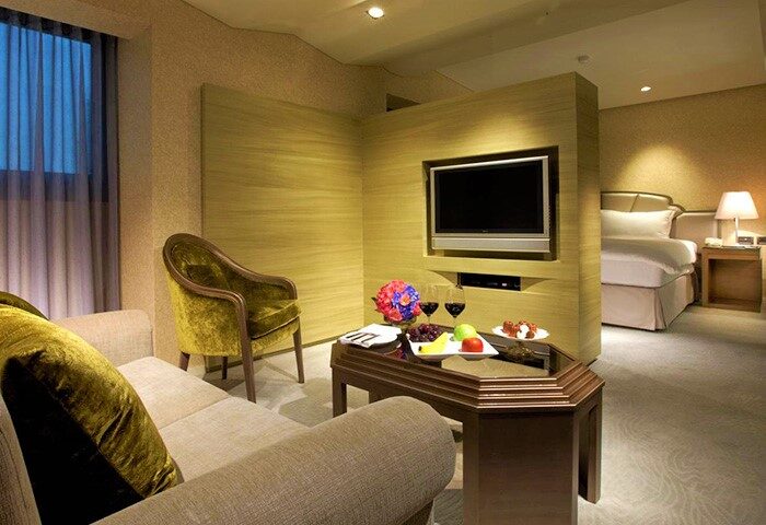 The Landis Taipei Hotel suite. Gay-friendly hotel room featuring a seating area, TV, fruit plate, and a glimpse of the bedroom with a comfortable bed.