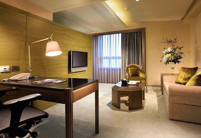 The Landis Taipei Hotel room interior. Desk, chair, TV, sofa, and flower arrangement. Gay-friendly hotel in Taipei, Taiwan. Upscale travel.