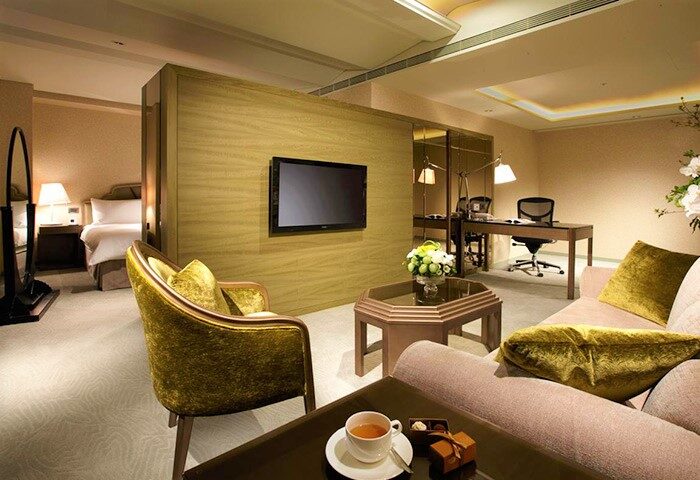 The Landis Taipei Hotel room. Gay-friendly hotel with living area, TV, desk, chair, sofa, and bedroom. Luxury accommodations in Taipei.