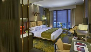 The Landmark Mandarin Oriental Hong Kong hotel room. Gay-friendly travel destination with a luxurious bed, desk, and city view.