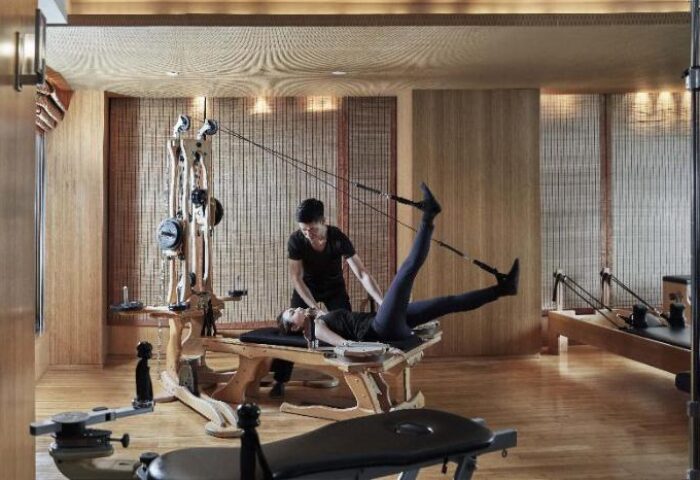 Gay-friendly The Landmark Mandarin Oriental Hong Kong gym. Woman using pilates equipment with trainer. Luxury hotel fitness center.