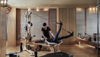 Gay-friendly The Landmark Mandarin Oriental Hong Kong gym. Woman using pilates equipment with trainer. Luxury hotel fitness center.