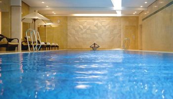 The Landmark Mandarin Oriental Hong Kong's indoor pool. A gay-friendly hotel with a man swimming. Sun loungers and umbrellas nearby.