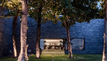 Exterior of The Library Hotel, a gay-friendly hotel. Lush trees frame the modern building with a welcoming, illuminated entrance.