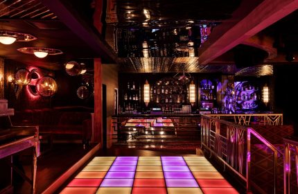 The LINQ Hotel and Casino gay-friendly bar. Dance floor with colorful lights, bar with bottles, and stylish decor. Gay travel advice.