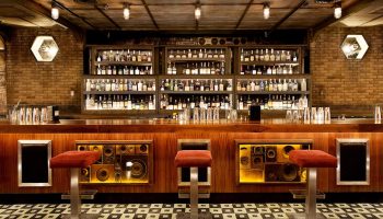 Bar at The Linq Hotel and Casino, a gay-friendly hotel. Speakers decorate the bar front. Bottles line the shelves. Stylish design.