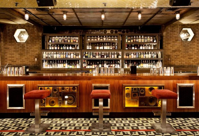 Bar at The Linq Hotel and Casino, a gay-friendly hotel. Speakers decorate the bar front. Bottles line the shelves. Stylish design.